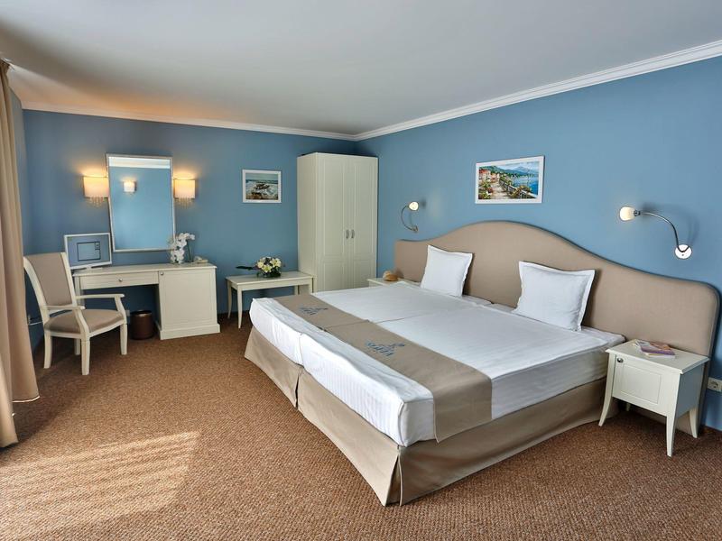 Habitación de hotel luminosa con cama grande, escritorio, silla y paredes azules.