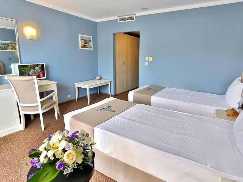 Habitación de hotel luminosa con dos camas individuales, escritorio, silla y decoración floral.