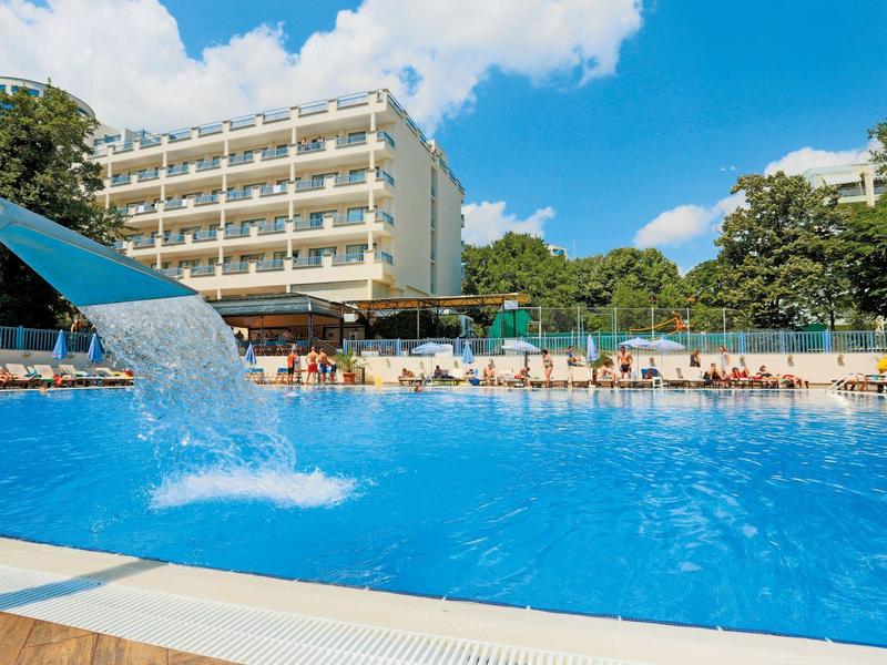 Gran piscina con tobogán de agua frente a un hotel de varios pisos bajo cielo azul.