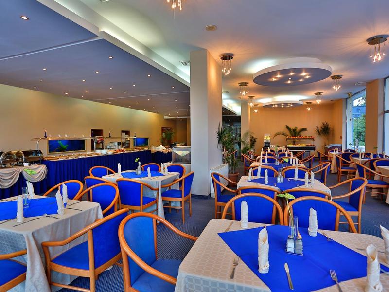 Amplio comedor de hotel con sillas azules, manteles blancos e iluminación moderna.