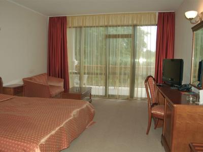 Camera d'hotel con letto matrimoniale, poltrone, scrivania, TV e finestra a tutta altezza verso il terrazzo.