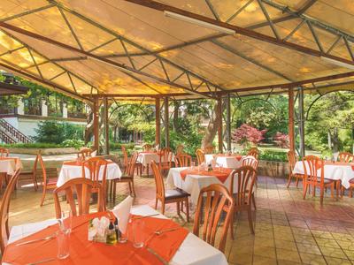 Überdachte Außenterrasse mit Tischen und Stühlen in einem Hotelgarten