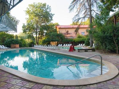 Piscina rotonda con lettini e vegetazione intorno in un giardino dell'hotel.