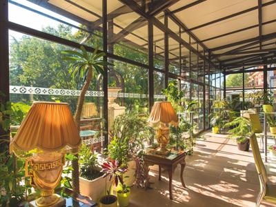 Heller Wintergarten mit Pflanzen, mehreren Lampen und Blick ins Freie unter einem Glasdach.