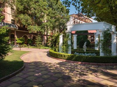 Gepflasterter Weg führt durch einen grünen Garten mit weißen Säulen und Hotelgebäude im Hintergrund.