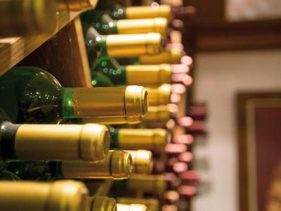 Scaffale con varie bottiglie di vino, alcune con capsule dorate, conservate affiancate.