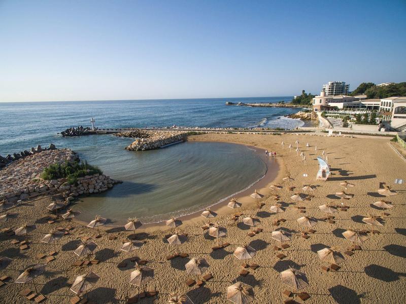 Spiaggia sabbiosa con lettini e ombrelloni accanto a una baia tranquilla e al mare sotto un cielo sereno.