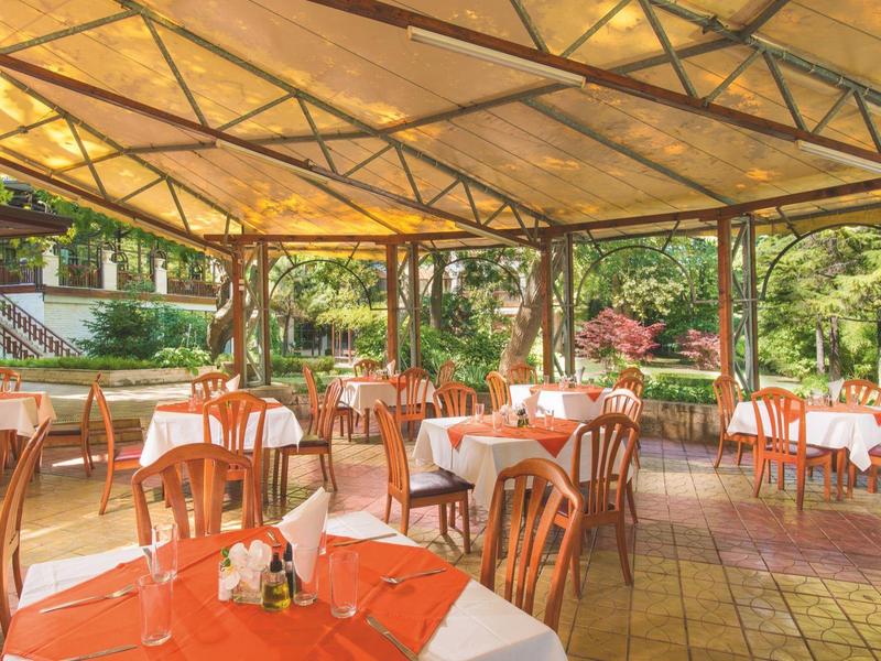 Terrazza esterna coperta con tavoli apparecchiati e sedie in legno in ambiente verde