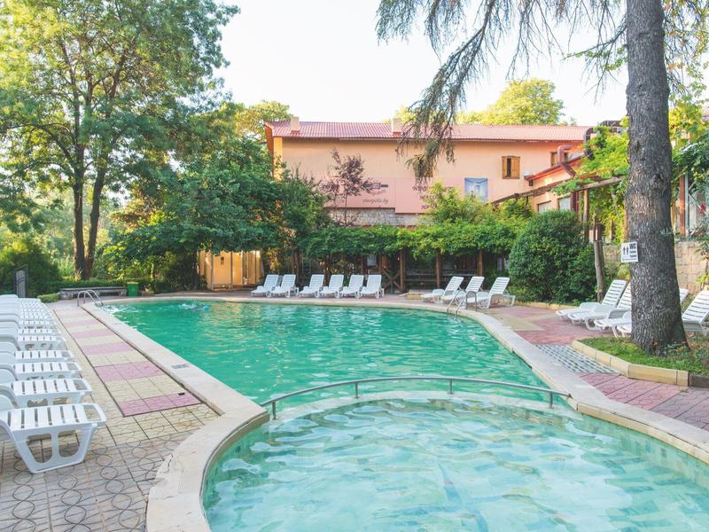 Vista di una piscina all'aperto con lettini bianchi e un edificio alberghiero rosa sullo sfondo.