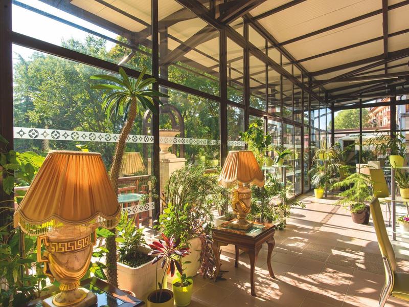 Terrazza soleggiata con molte piante, lampade e pareti di vetro in un hotel.