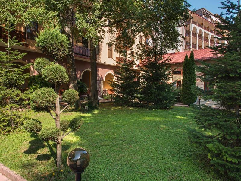Giardino verde con prato curato e alberi davanti a un edificio storico al sole.