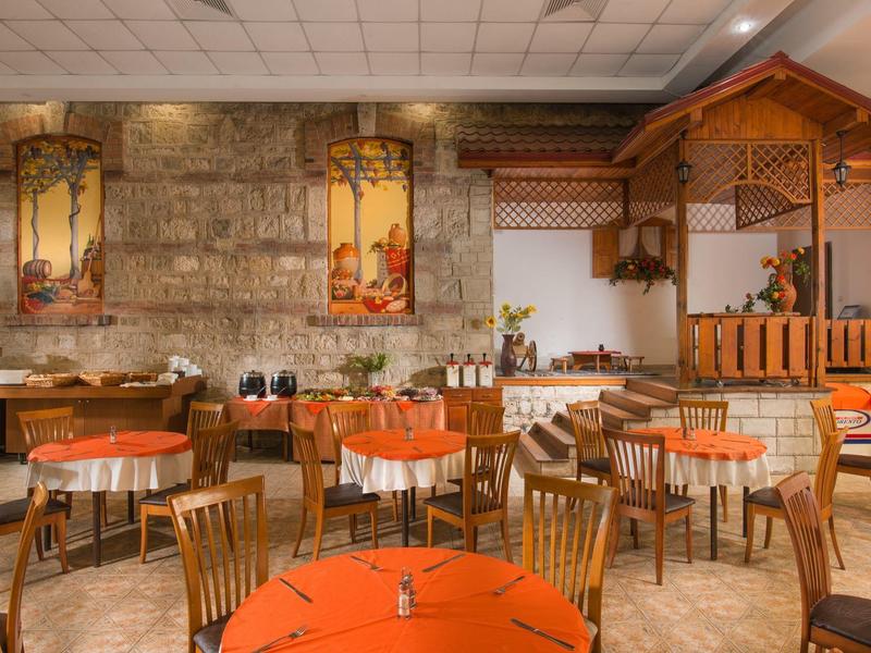 Accogliente area ristorante dell'hotel con tavoli rotondi e sedie in legno davanti a una parete in pietra naturale.