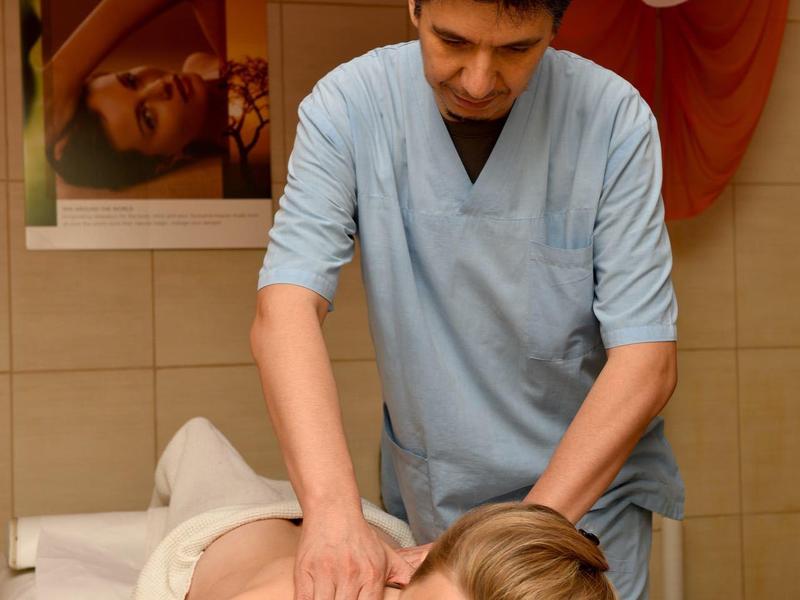 Un uomo massaggia le spalle di una donna sdraiata su un lettino da massaggio.