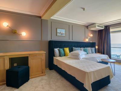 Camera d'albergo moderna con due letti, zona salotto e vista mare attraverso ampie finestre.