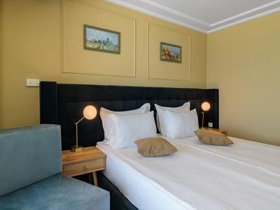 Camera d'hotel accogliente con letto matrimoniale, comodini e area salotto in tonalità calde di giallo.