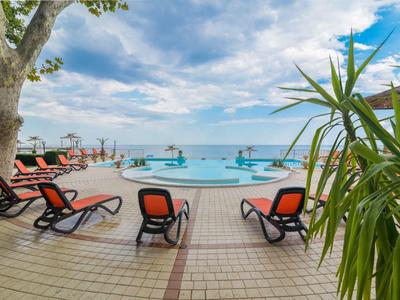 Poolbereich mit Liegestühlen und Blick auf das Meer unter einem bewölkten Himmel.
