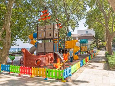Parco giochi colorato per bambini con struttura per arrampicata e scivolo vicino a una riva in ambiente urbano.
