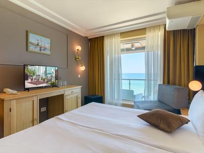 Modernes Hotelzimmer mit Doppelbett, Fernseher, Tisch und Balkon mit Meerblick.