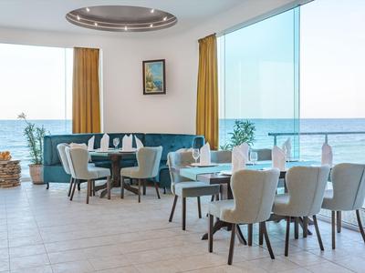 Helles Hotelrestaurant mit Sitzgruppen und großem Panoramafenster mit Meerblick.