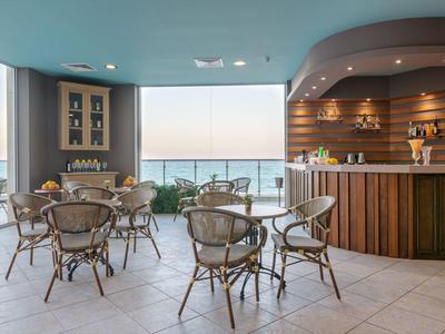 Offener Hotelbarbereich mit Weitblick aufs Meer, Holztheke und Rattanstühlen.