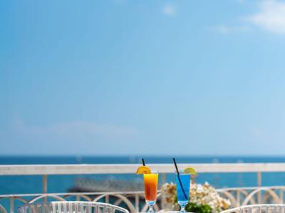 Blick auf Terrasse mit weißem Gartentisch, Stühlen und Sonnenschirm am Meer.