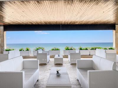Moderner Lounge-Bereich mit weißen Möbeln, blickt auf das Meer unter blauem Himmel.