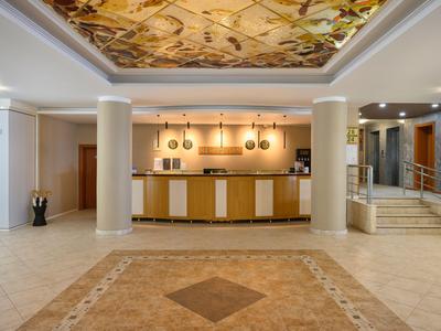 Ein heller Hotel-Lobbybereich mit Rezeption, dekorativer Decke und Marmorboden.
