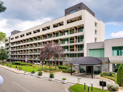 Großes modernes Hotel mit mehreren Etagen und Balkonen in grüner Umgebung.