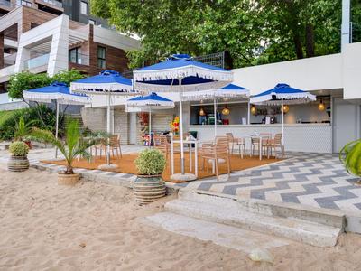 Strandbar mit blauen Sonnenschirmen und Holzmöbeln, direkt am Sandstrand gelegen.