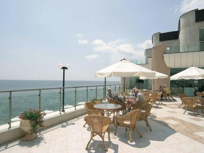 Terrazza con tavoli, sedie e ombrelloni con vista sul mare in una giornata di sole.