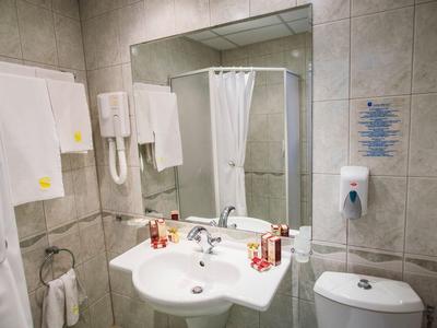 Bagno luminoso dell'hotel con lavabo, grande specchio, asciugacapelli e tenda della doccia.
