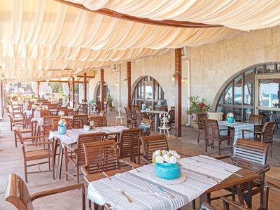 Terrazza esterna coperta di un ristorante con tavoli e sedie in legno sotto pannelli di tessuto bianco.