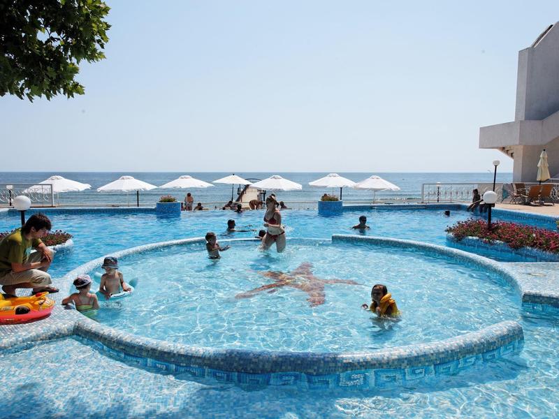 Persone che si godono una piscina con vista sul mare e ombrelloni bianchi sulla spiaggia.