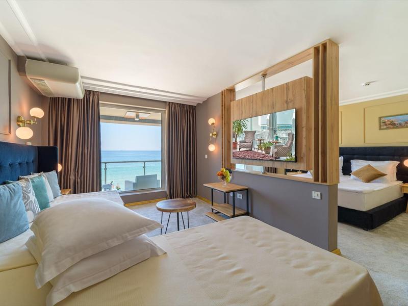 Camera d'hotel moderna con vista mare, letto, divano e balcone con tavolo e sedie.