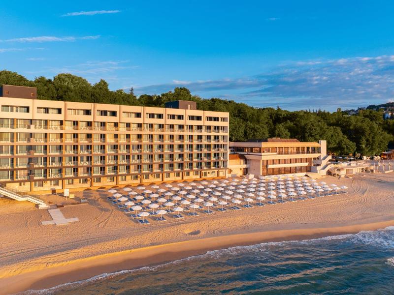 Grande hotel direttamente sulla spiaggia con lettini e mare calmo al tramonto.