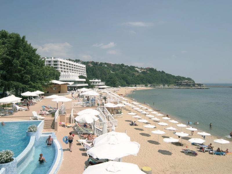 Hotel sulla spiaggia con ombrelloni, piscina e vista sulla costa in una giornata di sole.