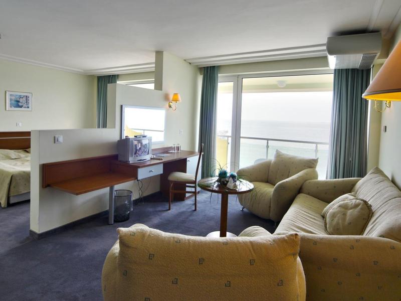 Camera d'hotel con letto, zona salotto, scrivania e grande finestra con vista sul mare.