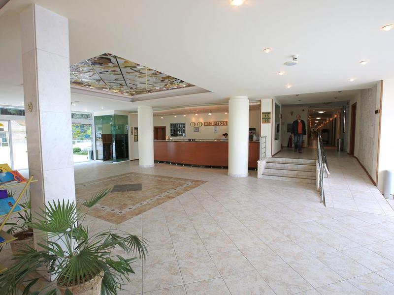 Luminoso atrio d'hotel con colonne, aree salotto e tappeto sul pavimento.