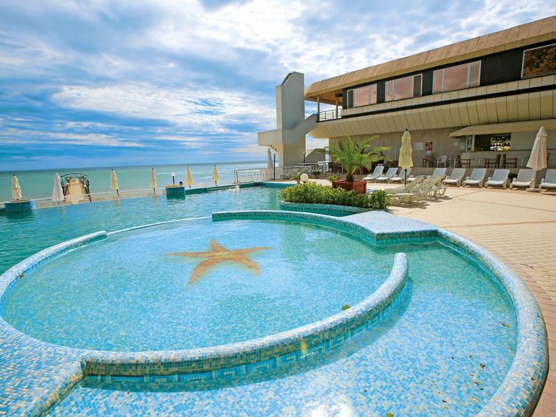 Piscina rotonda con motivo a stella accanto a una terrazza con lettini e vista sul mare.