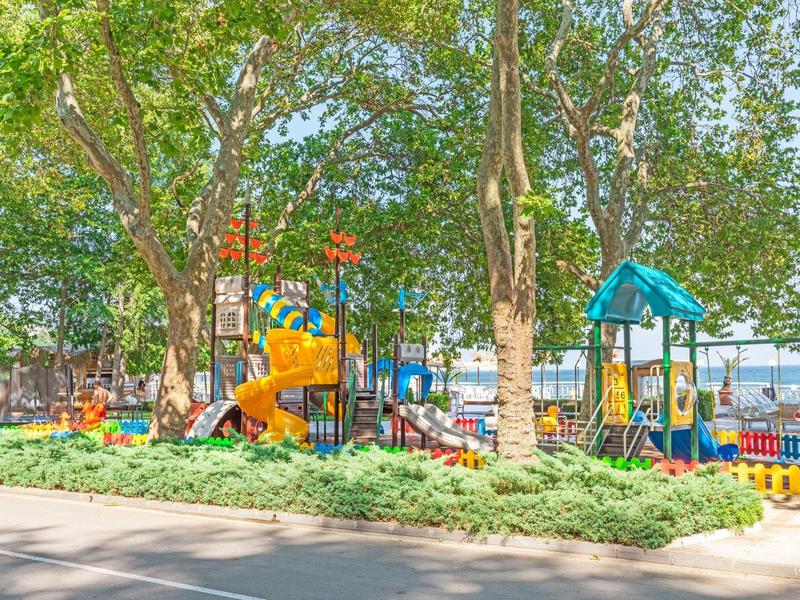 Parco giochi colorato con scivoli e strutture per arrampicarsi sotto grandi alberi in un parco.