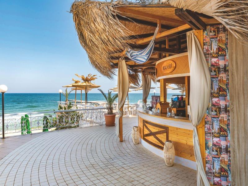 Bar sulla spiaggia aperta con tetto di paglia accanto al mare in una giornata di sole.