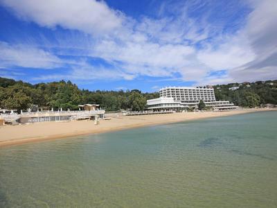 Beach with clear water and a large hotel building in the background under a blue sky.