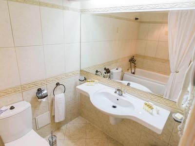 Bright bathroom with toilet, sink, and bathtub, light beige tiles on walls and floor.