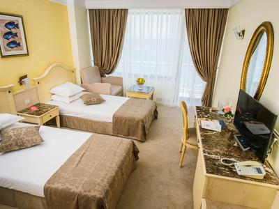 Bright hotel room with two single beds, chairs, and a desk with a TV.