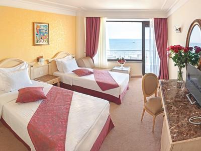 Hotel room with two single beds, TV, window with sea view, and roses on the table.