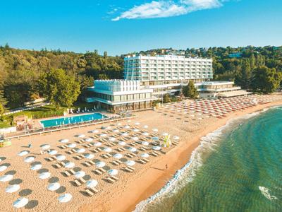 View of a beach hotel with sun loungers and umbrellas on the sandy shore next to clear sea.