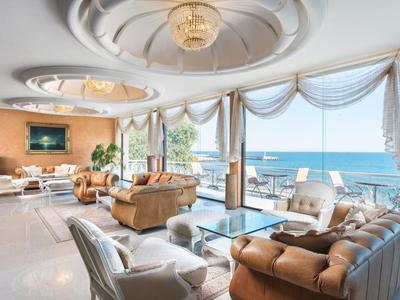 Bright hotel lounge with large windows, sea view, and elegant furnishings.