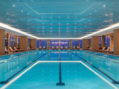 Moderne overdekte zwembad met blauwe verlichting en ligstoelen langs de zijkanten in een hotel.