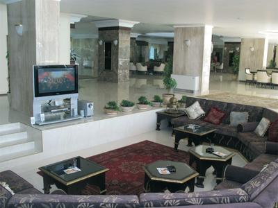 Bright hotel lobby with dark sofas, tables, and TV on a platform.
