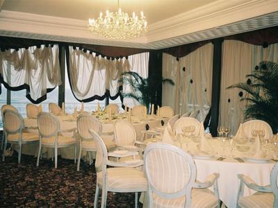 Elegant dining room with oval tables, white chairs, and chandeliers in a hotel.